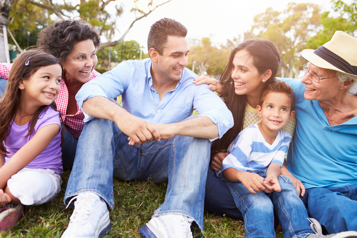 A Hispanic family sitting on the grass together smiling and happy