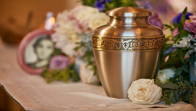 Flower engraved brass urn with a rose beside it sitting on a shelf at Pacific View