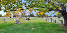 Cemetery grounds with headstones and a flat marker under a tree at Resthaven Memorial Park.