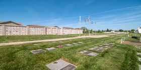 Cemetery grounds with top view of the flat markers and a mausoleum in the background with flags and flag poles at Mount Vernon Memorial Park & Mortuary.