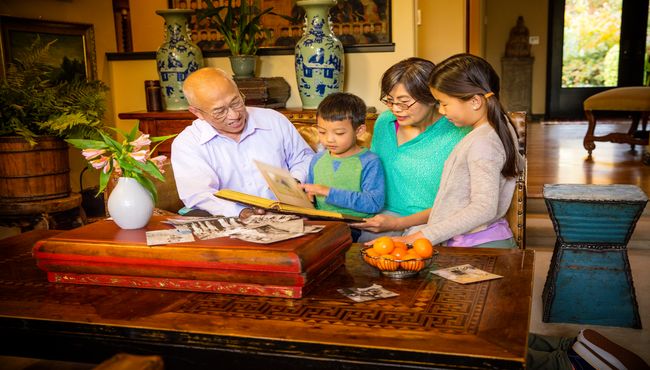 Grandparents and Grandchildren look through old photographs in the living room. 