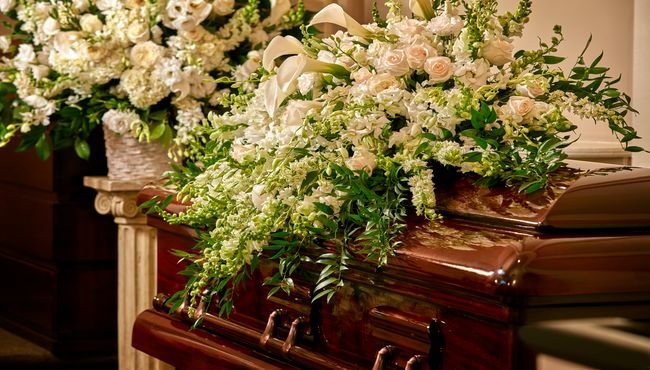 Spray of white roses and tulips laid on top of a wooden casket inside Frank E. Campbell Funeral Chapel.