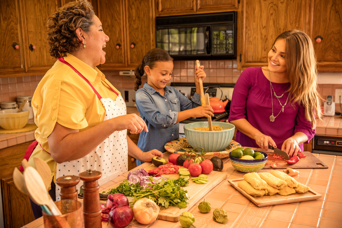 A multi-generational family stands at a kitchen island and cooks a healthy meal together.