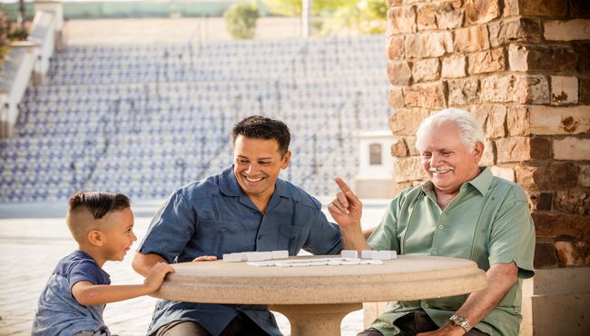 A grandfather sits with his son and grandson in an community cemetery.