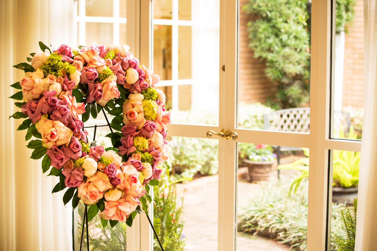 Rose floral heart-shaped wreath on stand facing window.