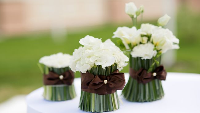 White roses tightly bundled in silky, brown ribbon create a simple and elegant centerpiece.  
