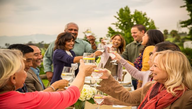 A group of people raise their glasses to toast to a loved one at an outdoor celebration. 