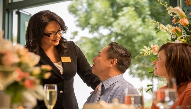 A female Dignity Memorial associate smiles as she talks to an Asian man with her hand on his shoulder. 