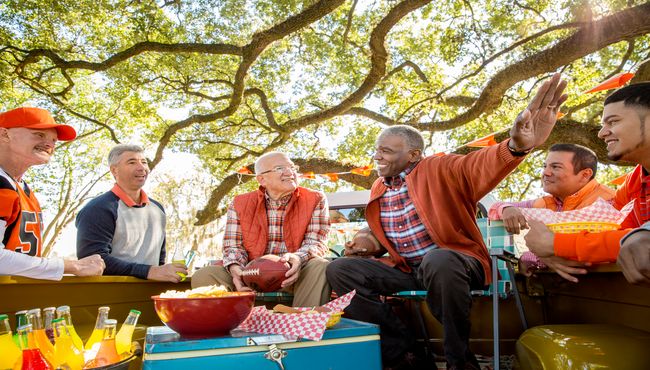 A group of men sitting around and visiting at a celebration tailgate.