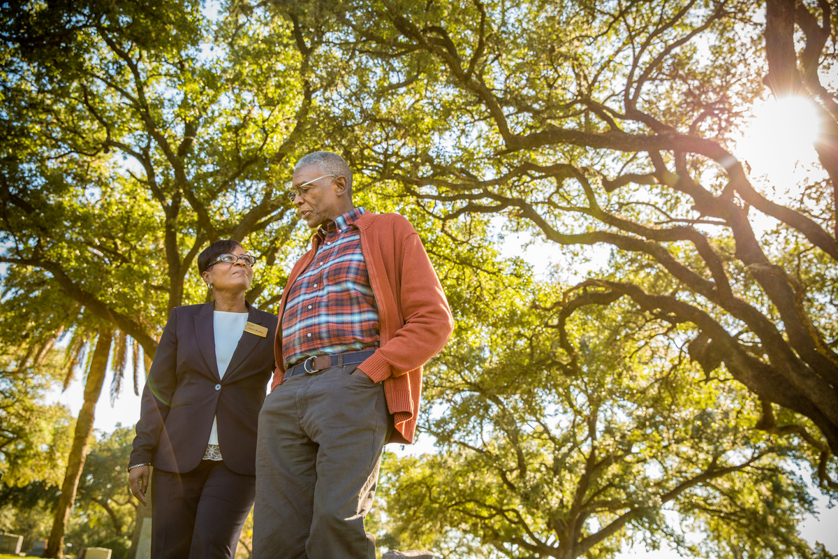 A Dignity Memorial associate looks at a gentlemen as he talks and they walk through the cemetery with trees.