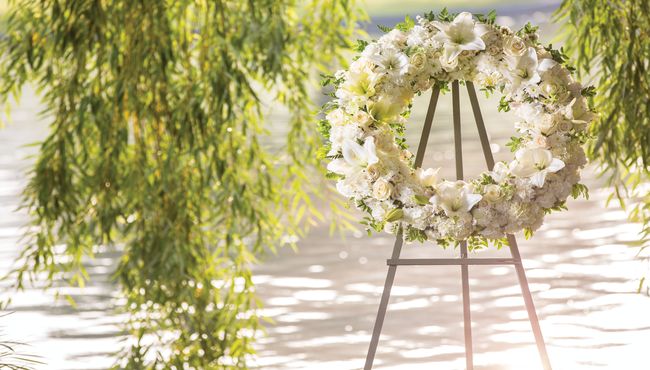 A white floral wreath near a willow tree and lake