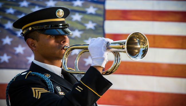 A man in uniform playing military bugle in front of American flag