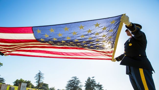 Soldiers in dress uniform stretch out the American flag in honor of the life of a fallen hero. 
