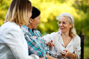 Three female friends sit outside smiling while having a conversation.