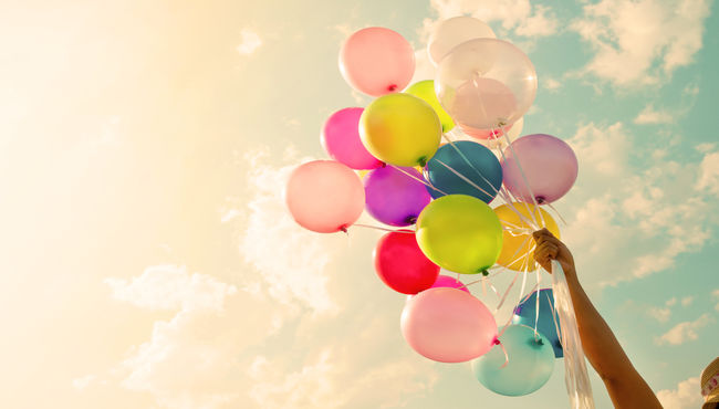 An arm holding a bunch of colorful balloons towards the blue sky