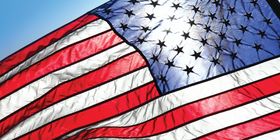 Close up of American flag flying in the sky with the sun behind it.