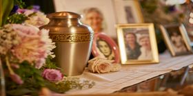 Brass urn with engraved flowers sitting on shelf next to flowers and framed pictures at Pacific View