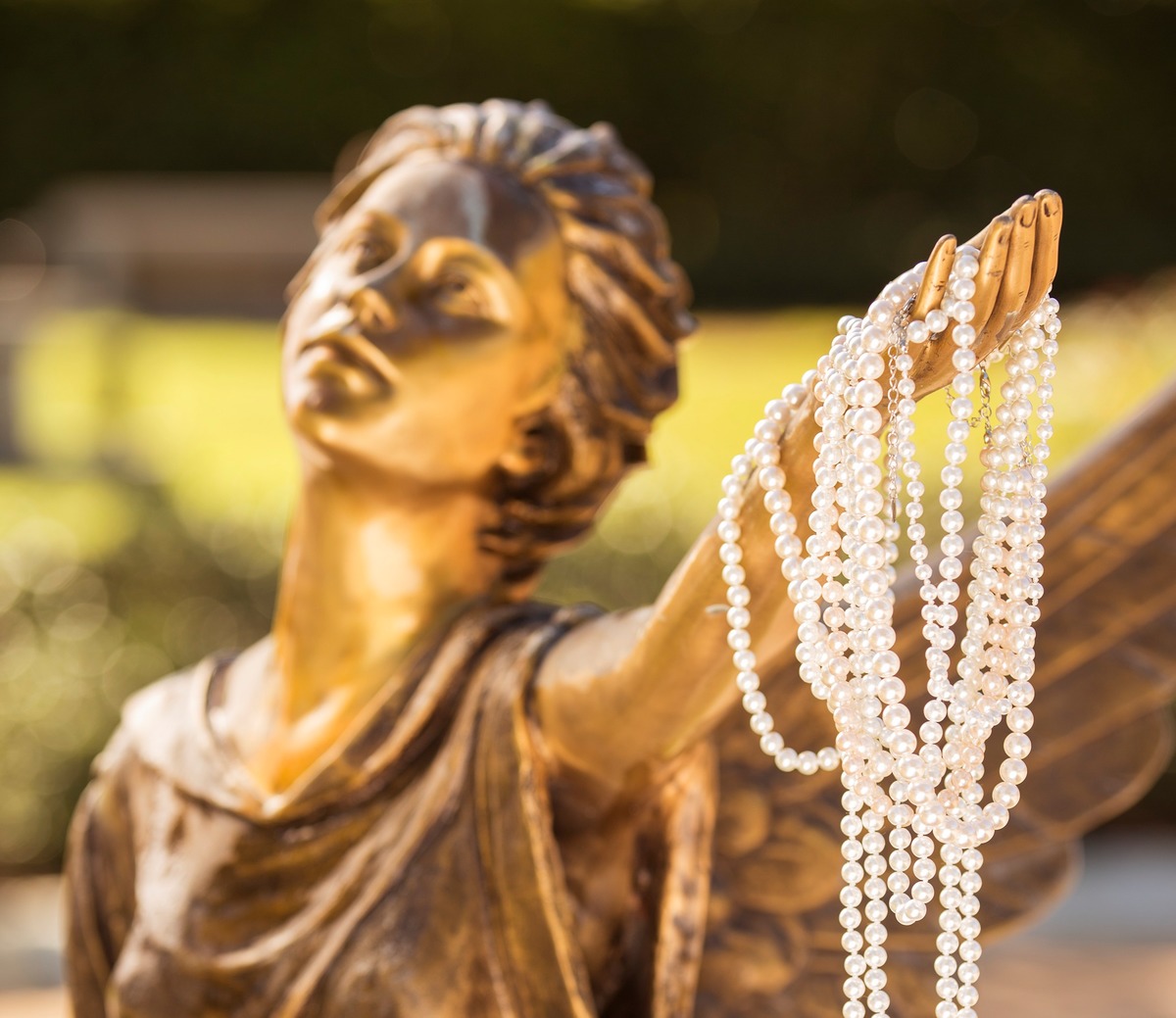 Bronze winged angel statue holding a string of pearls.