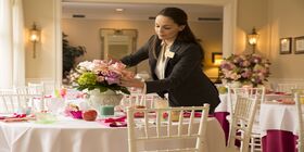 An associate arranges flowers on a table set for a reception.