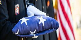 White gloved hands hold a folded American flag.