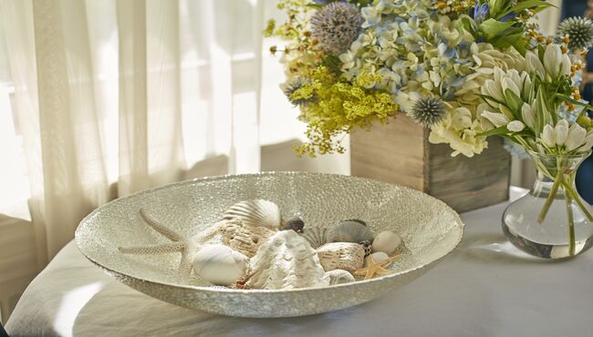 Shells in a glass bowl near a flower arrangement for a beach-themed life celebration. 