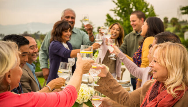 A group of people raise their glasses to toast to a loved one at an outdoor celebration.