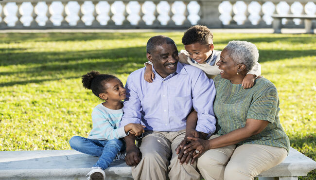 Grandparents sit with grandkids on a bench in a park