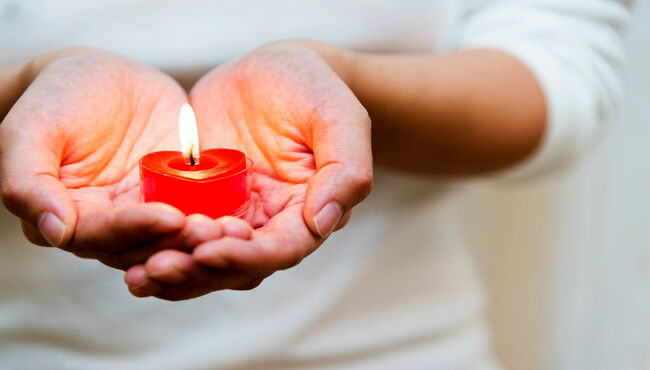 Woman hands holding burning heart-shaped candle