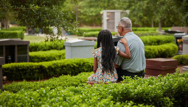 grandfather and granddaughter sitting on a bench in a cremation garden