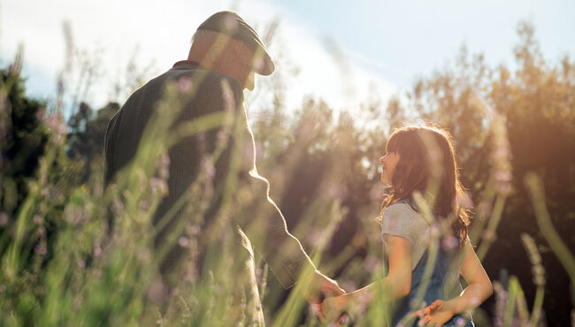 Grandfather and granddaughter holding hands in field