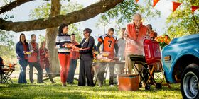 Group of people at a tailgate celebration cooking, eating and visiting.