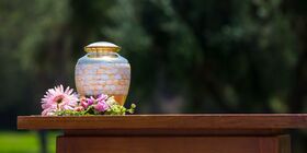 Urn outside on table with flowers around it