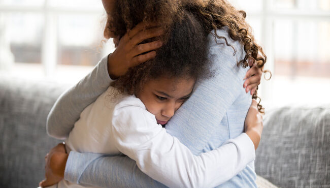 Black mother and daughter embracing sitting on couch