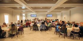A large celebration of life is hosted in a venue featuring round tables, a Memory Table, and many guests