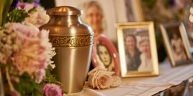Brass urn with engraved flowers sitting on shelf next to flowers and framed pictures at Pacific View