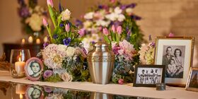 Display table with brass urn, pictures, flowers and glowing candle sitting on top of it at Pacific View