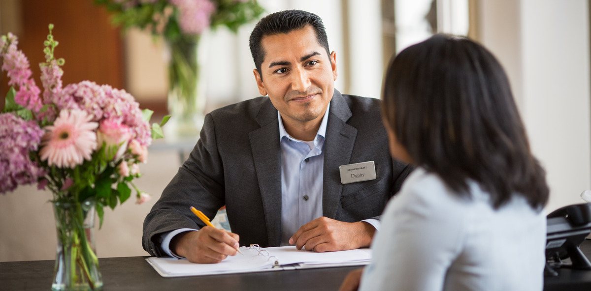 A Dignity Memorial associate speaking with a client while sitting at a desk. 