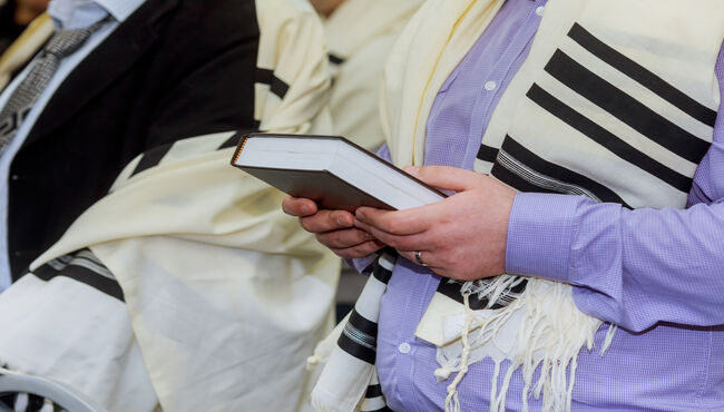 Hands holding a jewish prayer book wearing a prayer shawl