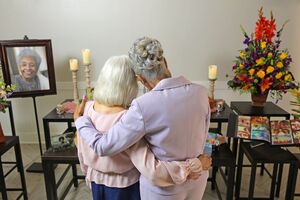 Friends comfort one another at a funeral reception near a table display honoring their loved one