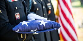 White gloved hands hold a folded American flag.