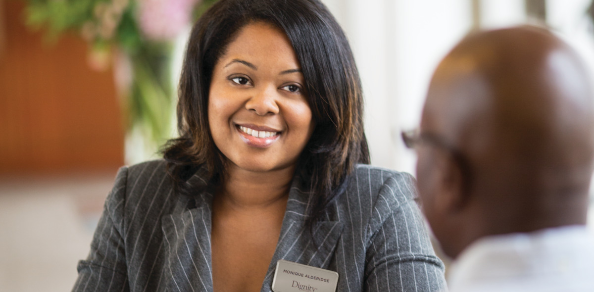 A Dignity Memorial associate speaking with a client while sitting at a desk. 