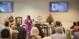Seated guests listen to a celebrant speak at a funeral reception