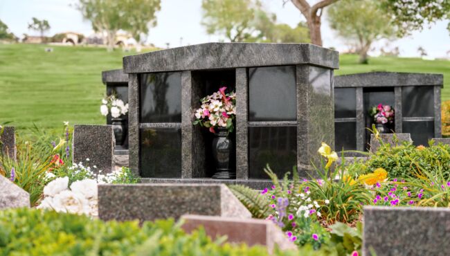 Scenic pathway in the cremation garden featuring columbariums, flowers, green grass, and trees.