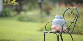 A cremation urn sits on a metal chair with flowers