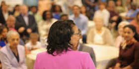 A celebrant speaks to a crowded room during a celebration of life