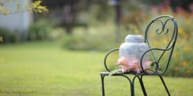 A cremation urn sits on a metal chair with flowers